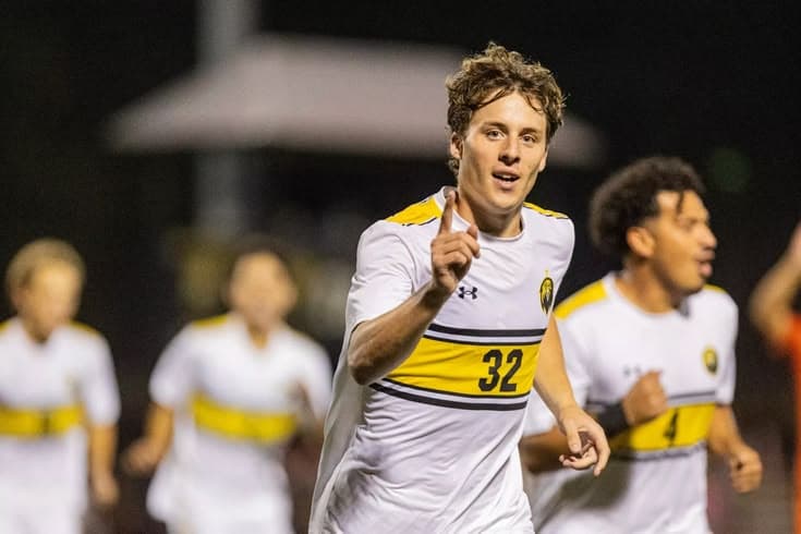 Joueur en tenue blanche et jaune levant la main sur un terrain de football